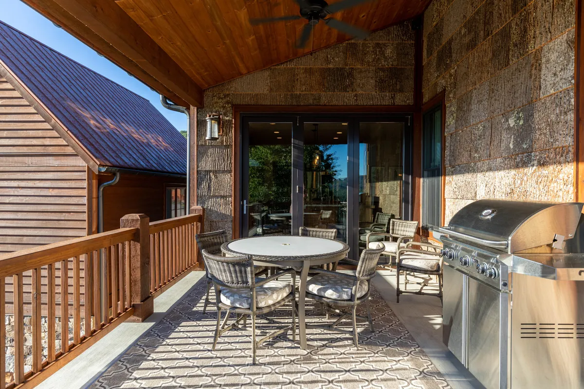 A spacious outdoor deck equipped with a dining table, woven chairs, and a modern grill, framed by a wooden railing and open to the surrounding natural landscape. This inviting space is ideal for outdoor meals, barbecues, and gatherings with friends or loved ones.