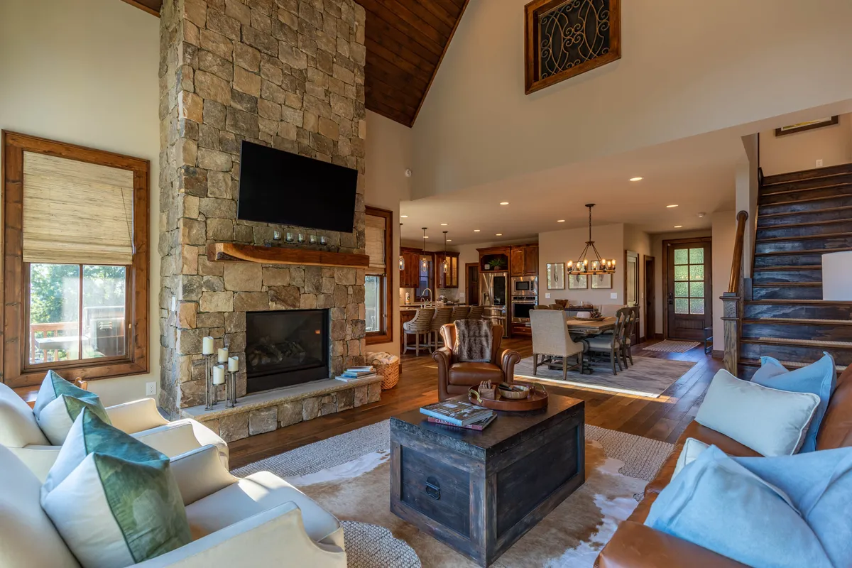 A spacious, open interior view showcasing the stone fireplace, central coffee table, inviting sofa seating area, and dining space, all unified within an open-concept layout ideal for family gatherings and social events.