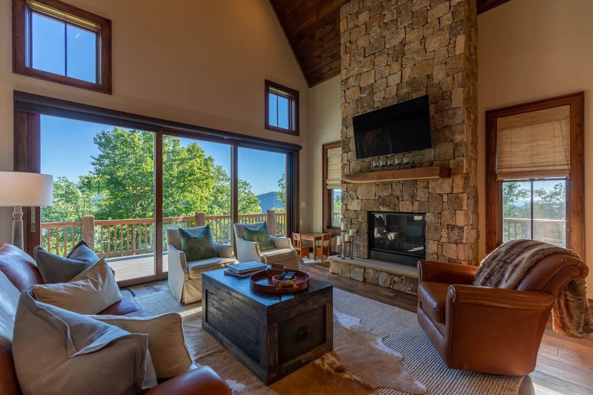 This image captures a warm and welcoming living room with a custom stone fireplace, large windows framing mountain views, and plush seating that invites relaxation and conversation.