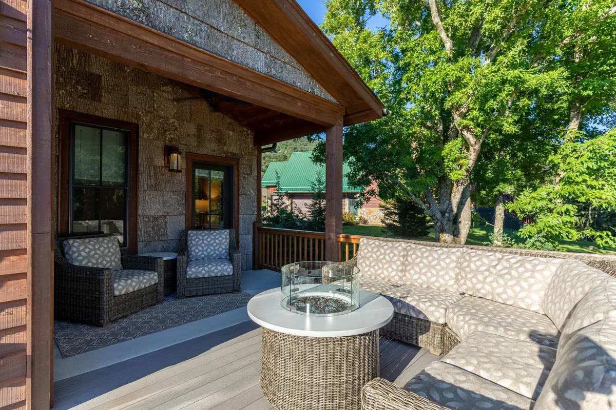 A stylish outdoor seating area featuring a curved sofa around a circular coffee table, surrounded by lush greenery. Soft sunlight filters through the nearby trees, creating a tranquil setting perfect for relaxing, enjoying nature, or socializing at sunset.
