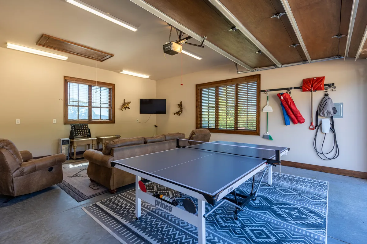 A vibrant interior setup with a ping pong table, cozy seating area, blinds drawn over several windows, and a television mounted for easy viewing. The room feels optimized for recreation, blending space for active games and relaxed TV time.