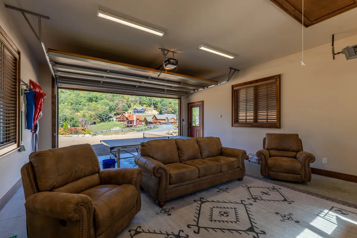 A cozy lounge area with brown leather sofas, an open garage door leading to panoramic landscape views, and plenty of natural light. The space invites relaxed gatherings, sunset watching, and casual camaraderie among friends.