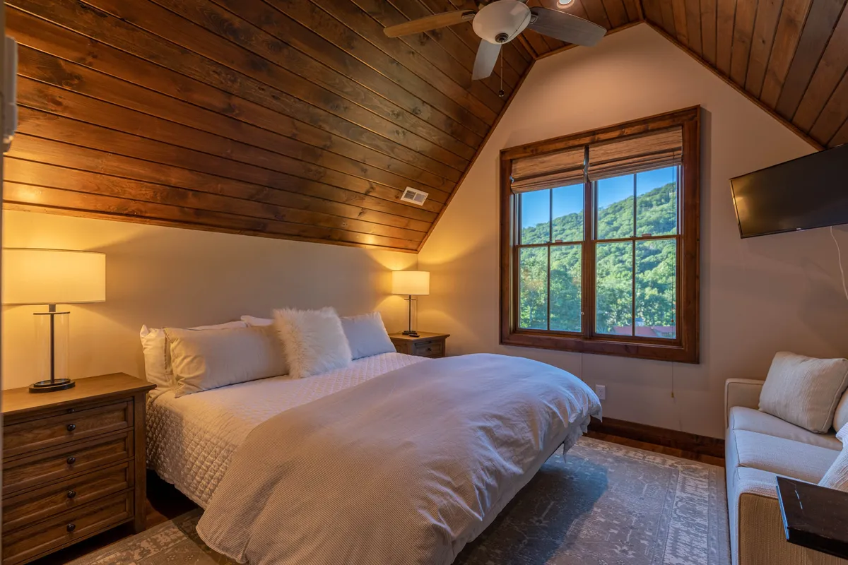 A tranquil bedroom with a bed, window letting in soft daylight, a nightstand, a sofa for lounging, and a ceiling fan. The arrangement suggests a comfortable, restful environment ideal for winding down.