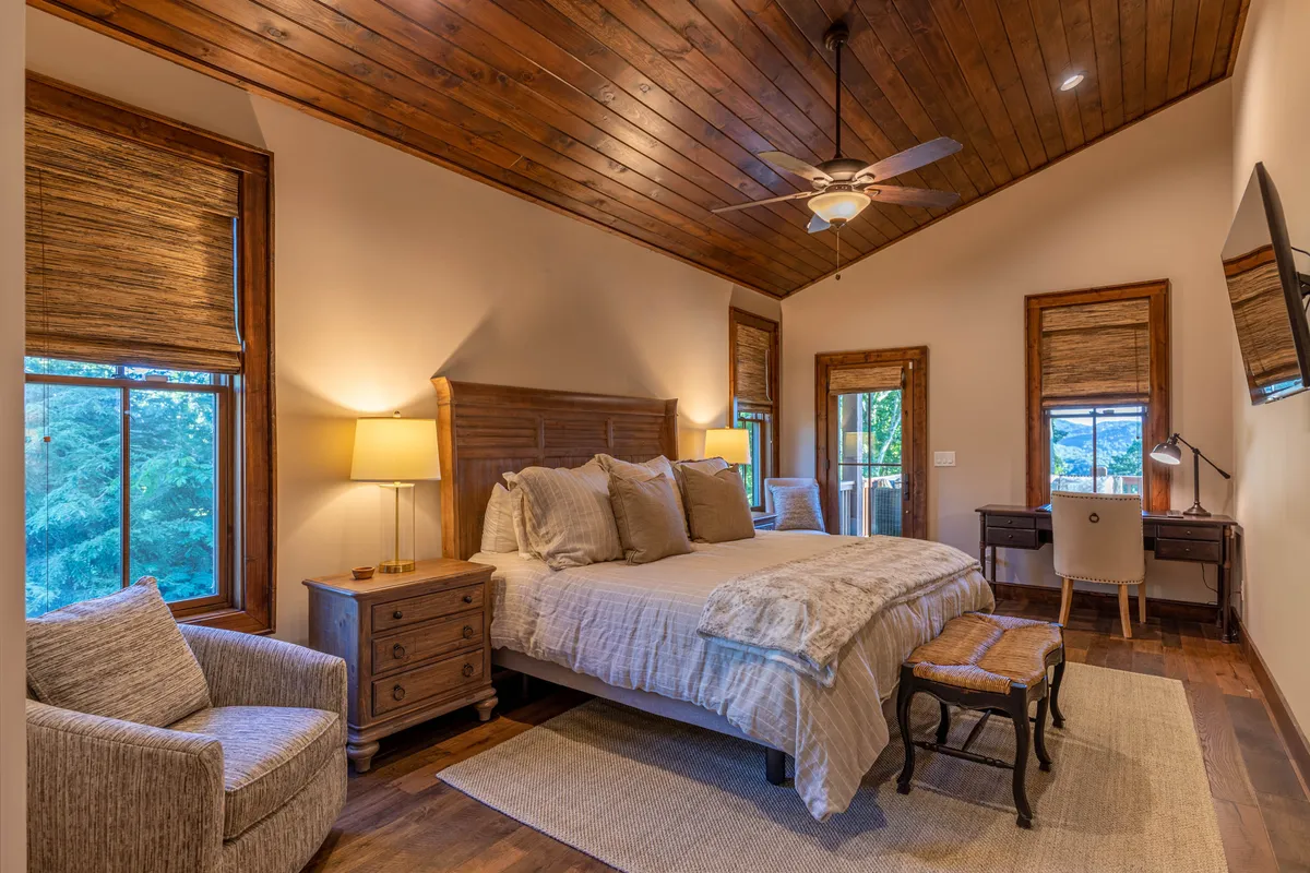 A bright bedroom with a bed, comfortable armchair, desk, and large windows that let in natural light. The seating area and workspace provide both comfort and utility for guests seeking a quiet escape.