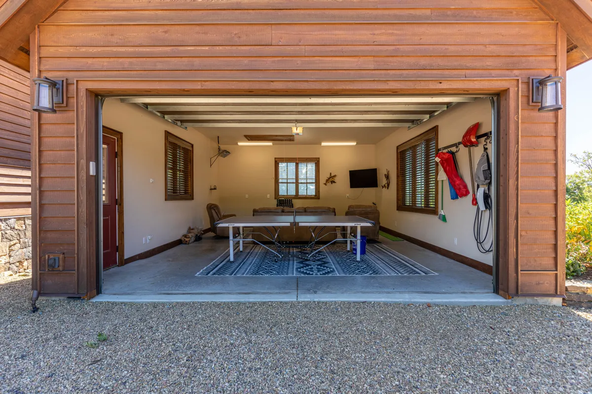 A spacious garage game room featuring a ping pong table positioned at the center, comfortable seating arranged nearby, and a large window that lets in natural light and offers a glimpse of the outdoors. The atmosphere is casual and inviting, ideal for family game nights or friendly competitions.