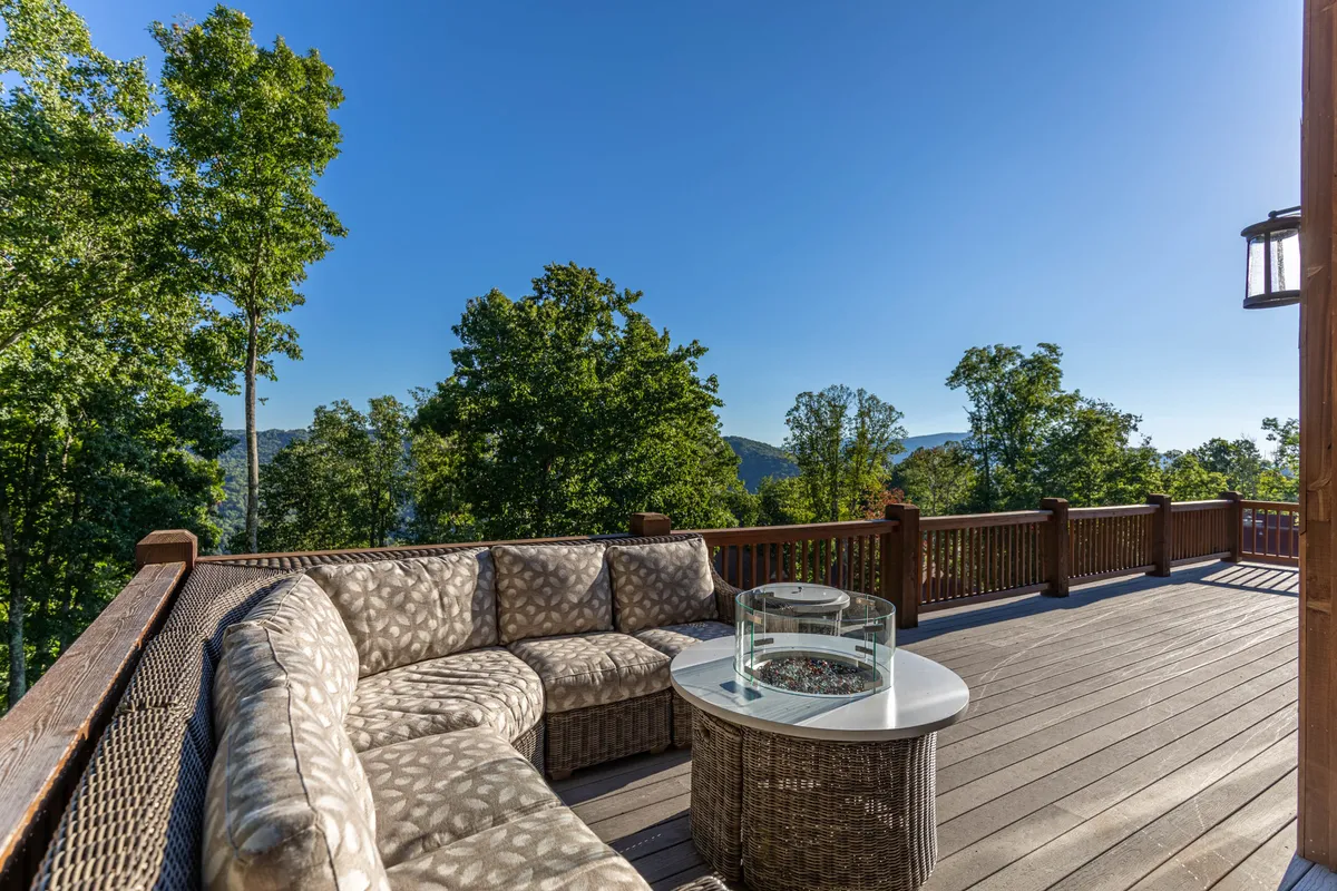 An inviting outdoor fire pit area surrounded by comfortable seating, ringed by trees and with a backdrop of scenic mountain views. The setting is ideal for evening gatherings, storytelling, or roasting s’mores under the stars.